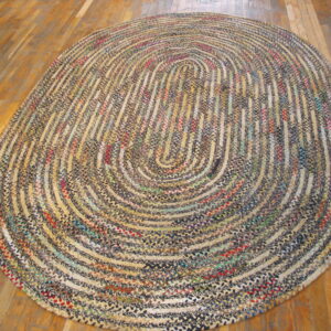 A large braided oval rug in multicolor tweed patterns rests on polished wood floorboards.