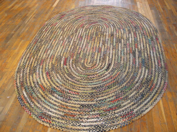 A large braided oval rug in multicolor tweed patterns rests on polished wood floorboards.