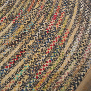 Close-up shows a highly textured rug featuring curved bands of light and dark specks with red and blue accents.