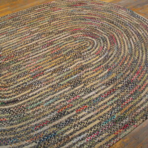 A multicolored, braided oval rug with concentric rings of tan and dark colors rests on wood flooring.