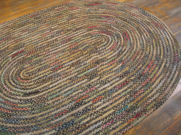 A multicolored, braided oval rug with concentric rings of tan and dark colors rests on wood flooring.