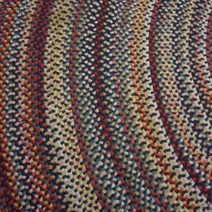 Multicolored braided rug featuring navy, red, and cream stripes on rustic wooden flooring.