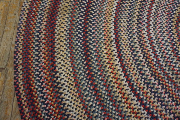 Multicolored braided rug featuring navy, red, and cream stripes on rustic wooden flooring.