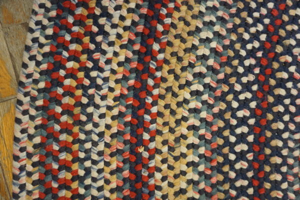 Braided rug in mixed navy, red, cream, yellow, and teal colors shown on wood flooring.