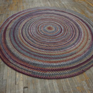 Multicolor braided round rug with concentric circles of red, blue, and beige on distressed wood planks.