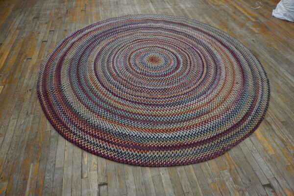 Multicolor braided round rug with concentric circles of red, blue, and beige on distressed wood planks.