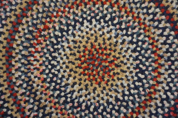Tightly braided multicolor rug texture with concentric rings of navy, red, cream, and tan fibers.