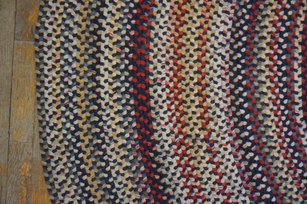 Braided rug texture shows navy, red, tan, and cream vertical stripes over gray wood planks.