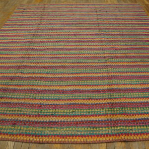 A multicolored braided rug with vibrant horizontal stripes lies on rustic wooden floorboards.