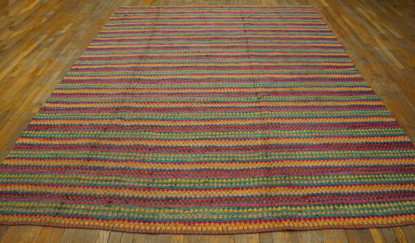 A multicolored braided rug with vibrant horizontal stripes lies on rustic wooden floorboards.