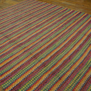 Vibrant multi-color flat-weave rug with diagonal stripes is displayed on rustic hardwood flooring.