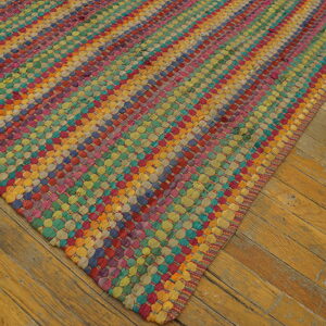 A multicolored, chunky woven rug featuring diagonal stripes rests on worn wood plank flooring.