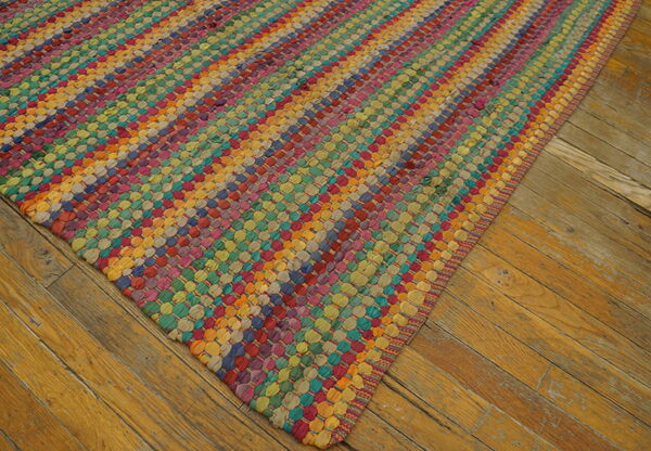 A multicolored, chunky woven rug featuring diagonal stripes rests on worn wood plank flooring.