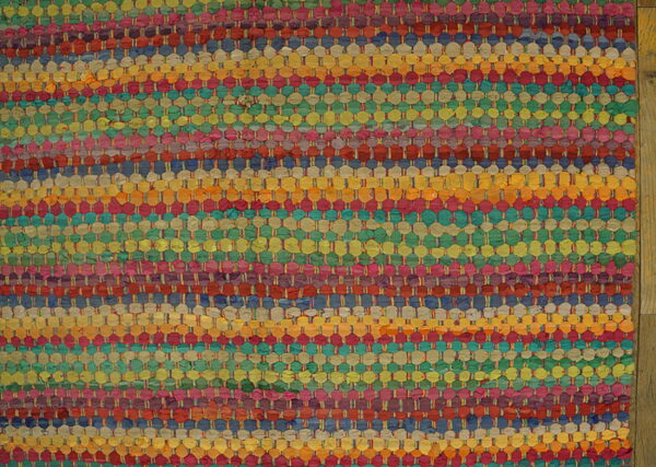 A vibrant, highly textured woven rug featuring horizontal stripes in bright multi-colors on wood flooring.