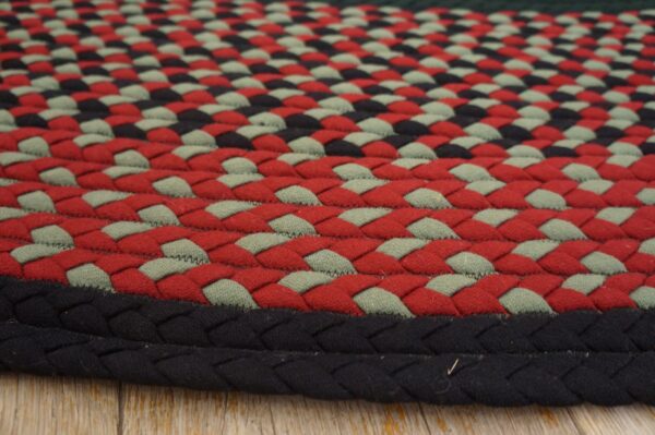 Braided rug featuring rows of red, sage green, and black stitches, resting on light wood floorboards.