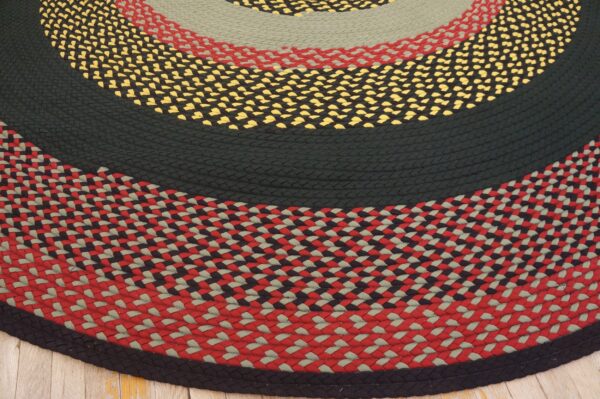Multicolored round braided rug featuring bands of solid black, sage green, red, and yellow checkerboard patterns over wood.