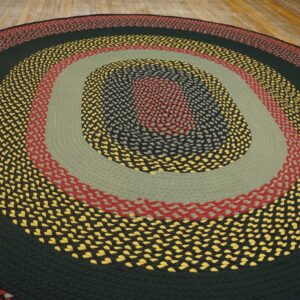 Multicolor braided rug with dark green, red, yellow, and sage concentric bands on wooden flooring.