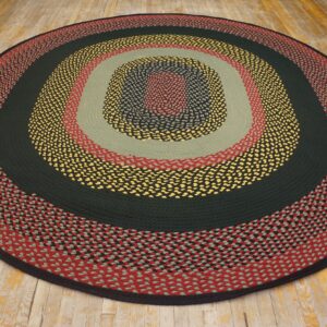 Round braided rug with concentric bands of red, sage, dark green, yellow, and black on wood flooring.
