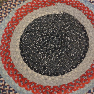 A round braided rug with concentric rings of speckled dark fabric, light gray, patterned red, and light blue.