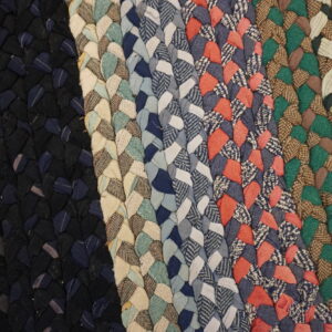 Close-up of a braided rug showing vertical stripes of various colors, including black, blue, cream, coral, green, and brown.