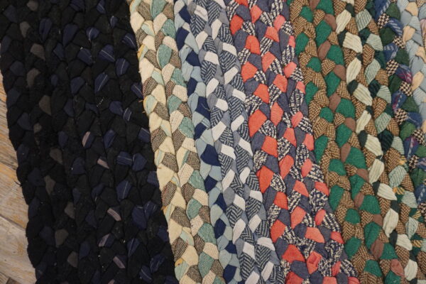 Close-up of a braided rug showing vertical stripes of various colors, including black, blue, cream, coral, green, and brown.