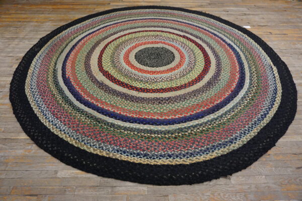 Round braided rug in variegated concentric colors, bordered in black, on a rustic wood floor.