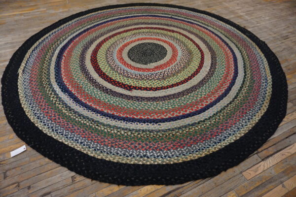 Circular braided rug with variegated rings of red, green, blue, and black rests on distressed wood flooring.
