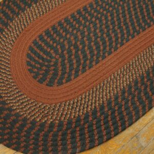 Braided oval rug in rust, black, and tan concentric patterns lying on distressed wood floor.