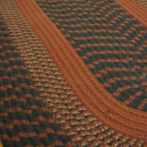 Braided area rug displaying rust, dark green, and tan color blocks on a distressed wood floor.