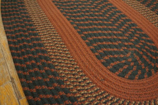 Braided area rug displaying rust, dark green, and tan color blocks on a distressed wood floor.