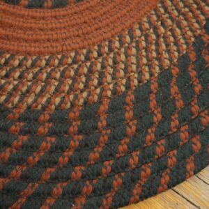 Braided rug in rust, tan, and dark green colors rests on distressed wooden floorboards.