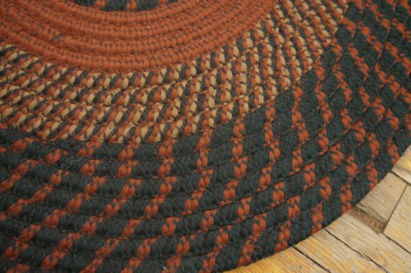 Braided rug in rust, tan, and dark green colors rests on distressed wooden floorboards.