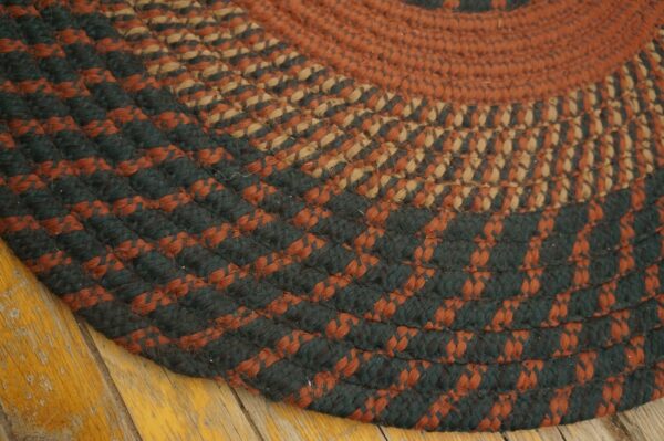 Close-up of a circular braided rug in concentric rings of rust, dark green, and tan over yellow wood floors.