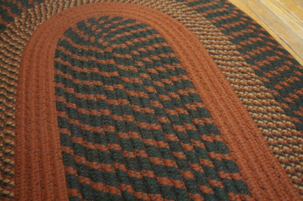 Close-up of a braided rug showing rust and dark green striped bands on light wood floor.