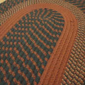 Rust, tan, and dark green braided rug with checkered bands rests on light wooden floorboards.