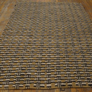 Tan, black, and white woven rug with a repeating geometric block pattern covers a wooden floor.