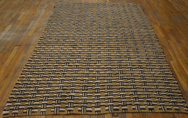 Tan, black, and white woven rug with a repeating geometric block pattern covers a wooden floor.