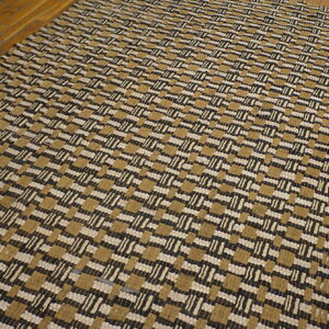Woven rug featuring alternating blocks and dashes in tan, cream, and dark brown on hardwood flooring.