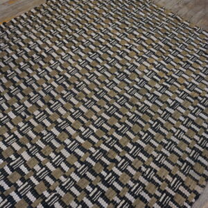 A low-pile woven rug featuring a black, beige, and off-white checkered pattern rests on gray wood flooring.