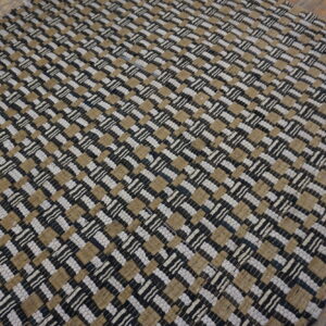 Textured black, tan, and white flatweave rug displaying a tight checkerboard pattern on wood flooring.