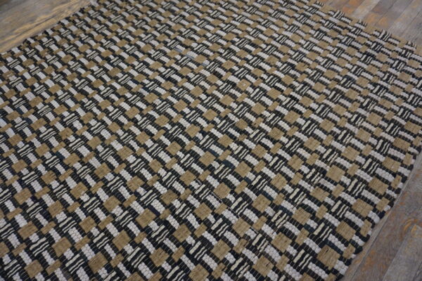 Textured black, tan, and white flatweave rug displaying a tight checkerboard pattern on wood flooring.