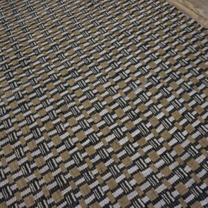 A black, tan, and white chunky flatweave rug rests on distressed wood planks.