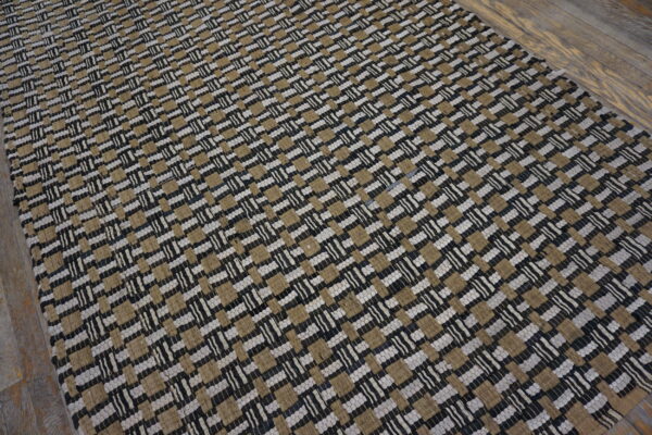 A black, tan, and white chunky flatweave rug rests on distressed wood planks.