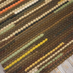 Textured rug with diagonal bobble stripes in earthy brown, olive, yellow, and orange on light gray wood floor.