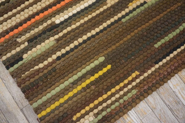 Textured rug with diagonal bobble stripes in earthy brown, olive, yellow, and orange on light gray wood floor.