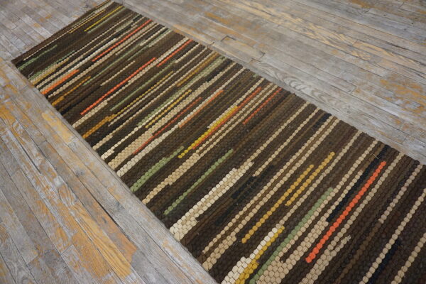 Brown, beige, and multicolored diagonal striped runner on a worn gray wood floor.