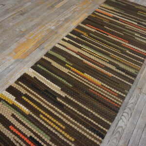 A narrow striped runner in browns, beige, olive, and orange sits on rustic whitewashed wooden planks.