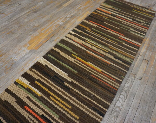 A narrow striped runner in browns, beige, olive, and orange sits on rustic whitewashed wooden planks.