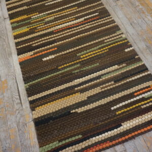 Dark brown, striped runner rug with multicolored accents on weathered gray wood flooring.