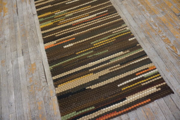 Dark brown, striped runner rug with multicolored accents on weathered gray wood flooring.